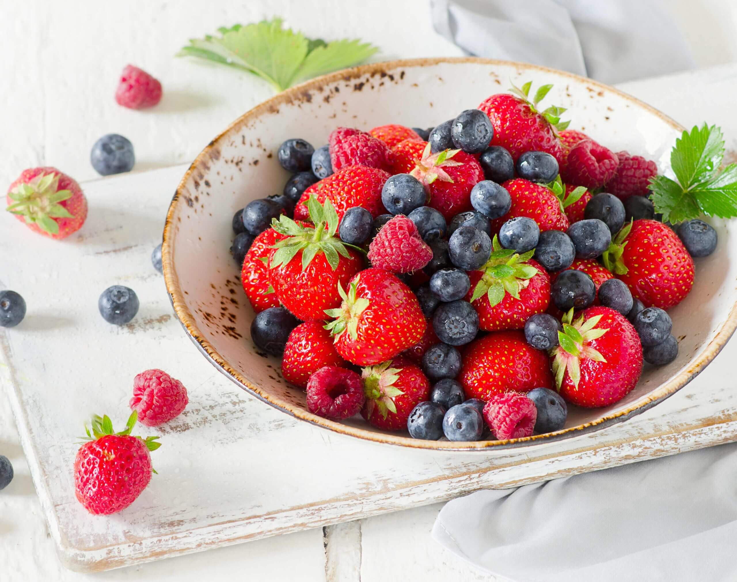 Eine weiße Schüssel mit Erdbeeren, Heidelbeeren und Himbeeren.