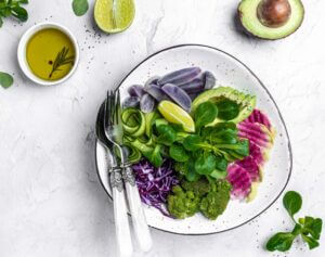 Ein Teller mit Vogerlsalat, Gurke, Broccoli, Rotkraut und Avocado garniert mit einer Scheibe Zitrone. Links am Teller liegen ein Löffel und eine Gabel.
