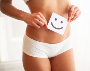 Eine Frau in weißer Unterwäsche die ein Bild vor ihrem Bauch hält auf dem sich ein Smiley befindet.