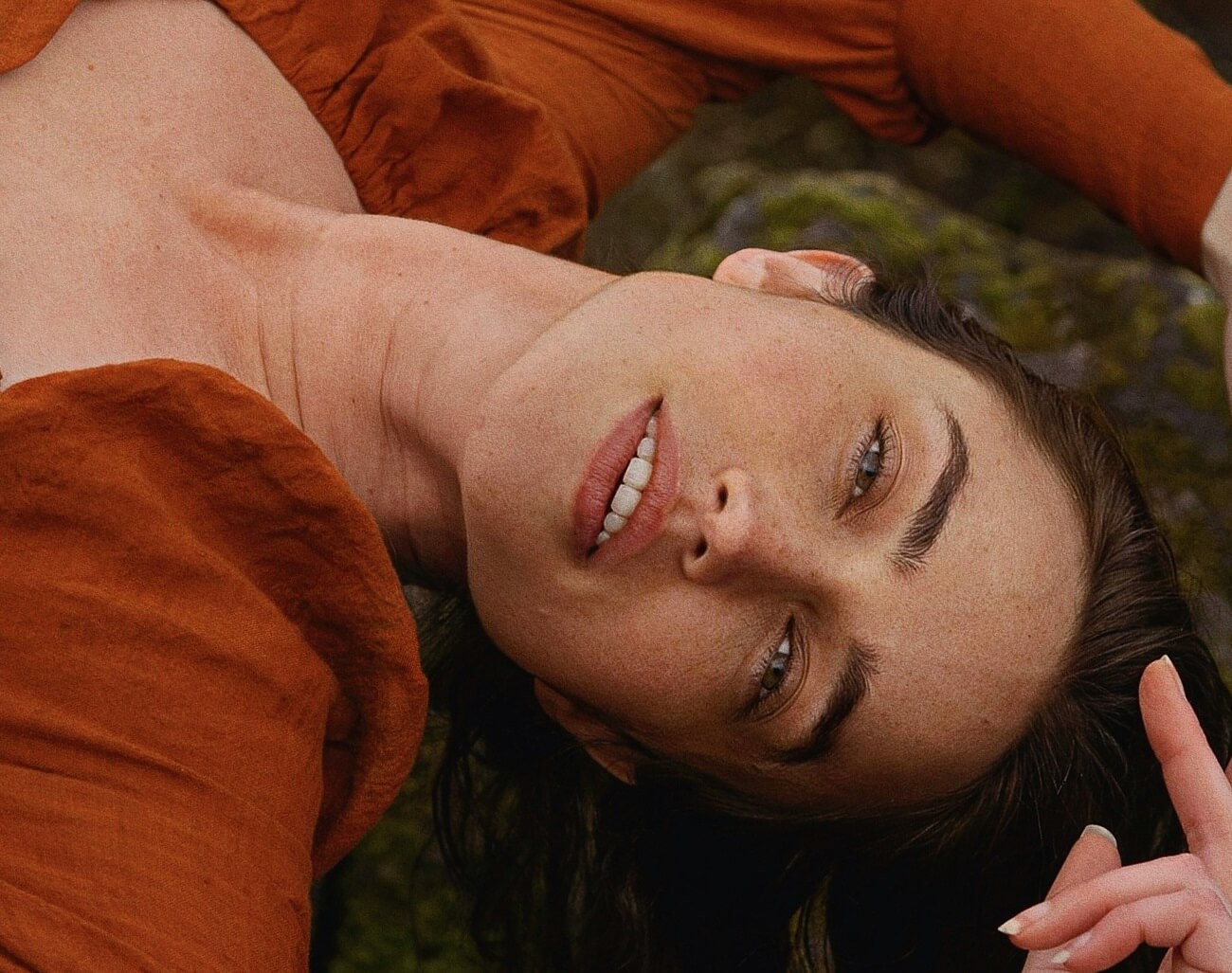 Frau mit Sommersprossen die eine orange Bluse trägt und lächelt.