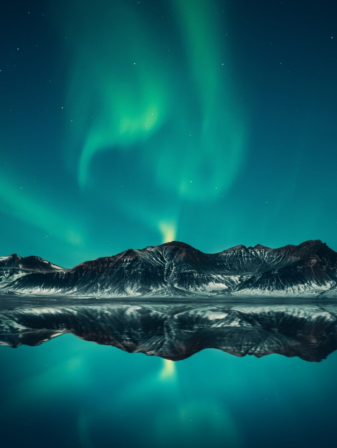 polarlichter-nordpol-bergkette-winter-tuerkis-atemberaubend-farbenspiel Am Himmel sind atemberaubende türkise Polarlichter zu sehen darunter eine beschneite Bergkette umgeben von einem kristallklaren See.