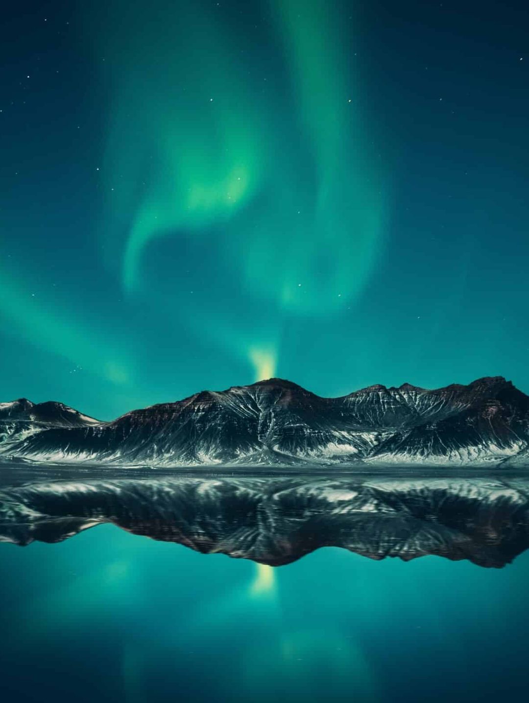 polarlichter-nordpol-bergkette-winter-tuerkis-atemberaubend-farbenspiel Am Himmel sind atemberaubende türkise Polarlichter zu sehen darunter eine beschneite Bergkette umgeben von einem kristallklaren See.
